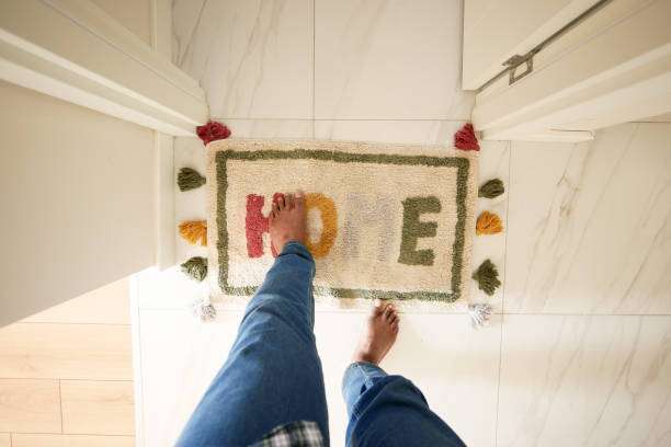 A rectangular rug with the word home written on it lays on the hardwood flooring in the hallway of the building,bath mat