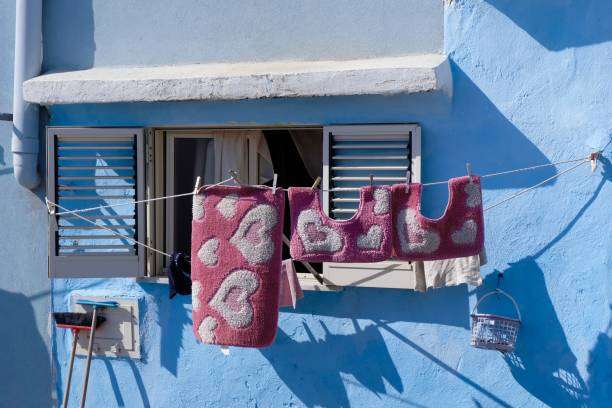 Pink heart-patterned bath mats drying on a clothesline outside a blue building.