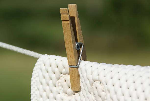 White textured bath mat drying on a clothesline with a wooden clothespin.