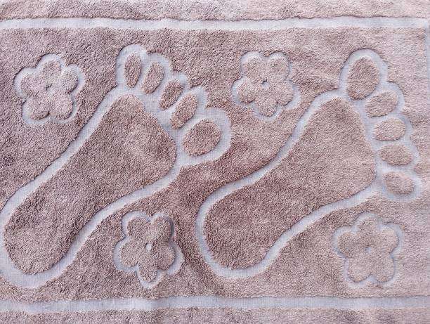 Brown textured bath mat with embossed foot sole and flower patterns for bathroom decor.