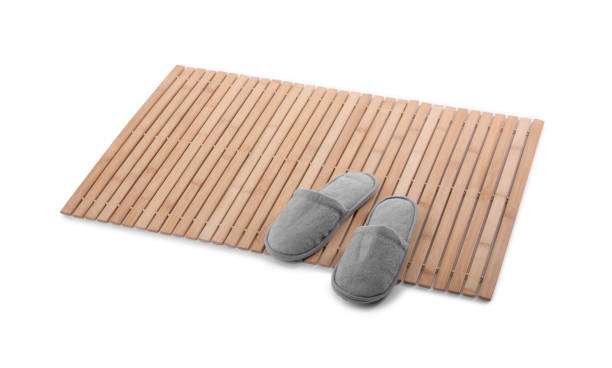 Bamboo bath mat with slippers on white background.