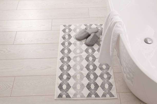 Soft bath mat with slippers next to a modern white bathtub.