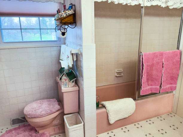 Pink vintage bathroom featuring toilet, shower, and a pink bath mat on the patterned floor.