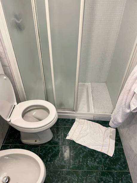 White bath mat on dark green tile floor in a small bathroom.