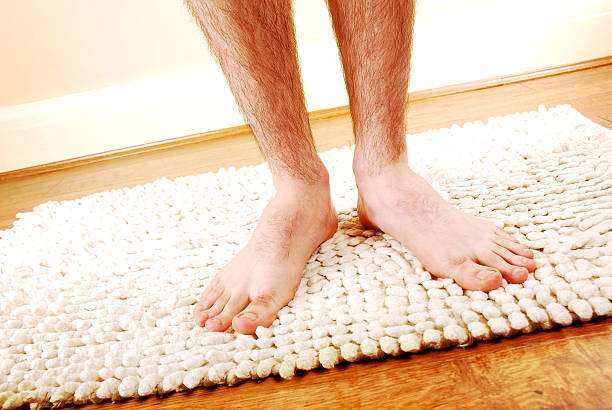 Bare feet standing on a soft, fluffy white bubble bath mat on a wooden floor.