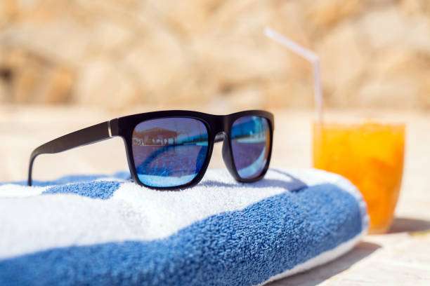 Sunglasses and drink on a striped towel, not a bath mat.