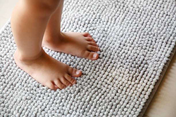 Child's bare feet stand comfortably on a plush, light grey shag bath mat.