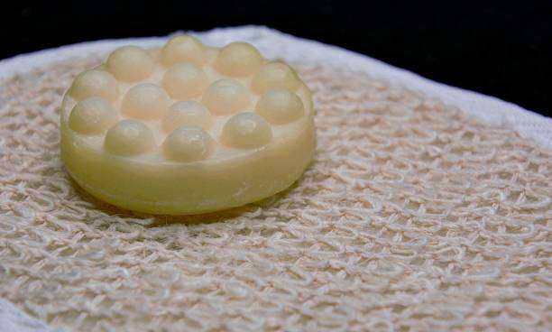 A white bar of soap with raised bumps sits on a textured beige bath mat.