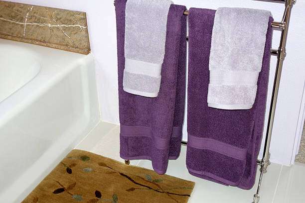 Brown floral bath mat next to purple towels.