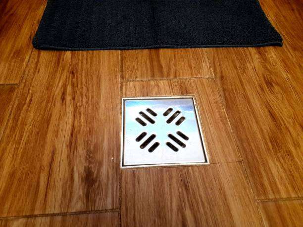 Black bath mat near shower drain on wood floor.