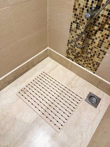 Modern shower with beige tiles, a sleek drain, and a wooden slatted bath mat.