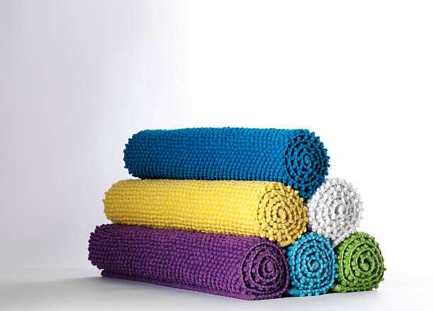 Stack of colorful rolled-up bath mats in blue, yellow, purple, white, green, and turquoise.
