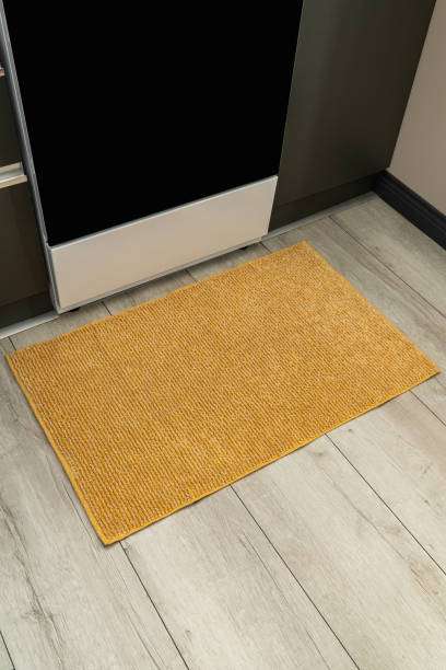 Yellow rectangular bath mat on light wooden floor next to a kitchen appliance.