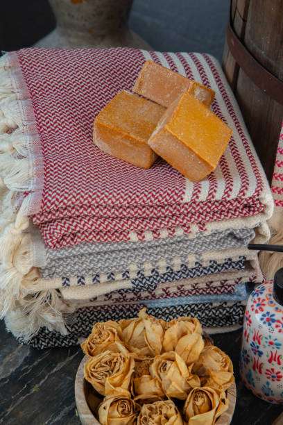 Stacked striped textiles resembling bath mats with fringes, topped with artisanal soap bars.