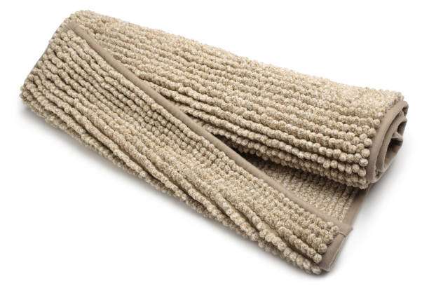 Rolled beige shag bath mat on white surface.