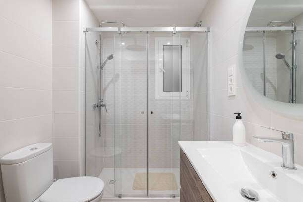 The spacious white ceramic tile bathroom is illuminated by bright white natural light. showing bath mat